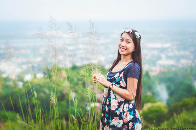 Portrait of happy woman holding plants while standing against landscape