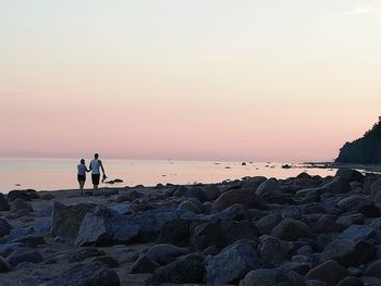 Men standing on rocks by sea against sky during sunset