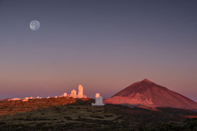 Observatory in teide nationalpark with volkano inthe back at sunrise with moon above.