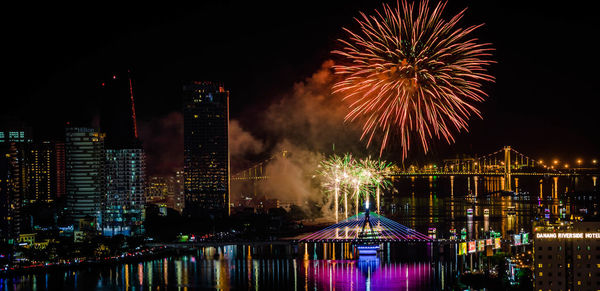 Firework display over illuminated buildings and river in city at night