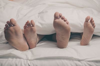 Low section of couple relaxing on bed at home