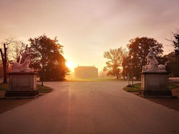 Road by trees against sky during sunset