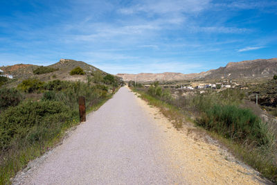 Road leading towards mountains against blue sky