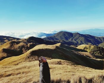 Side view of young woman looking up while standing against mountain ranges during winter