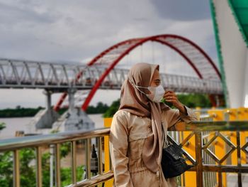 Rear view of woman standing against bridge against sky