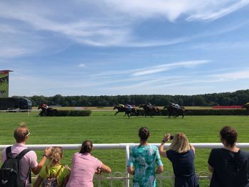 People watching horse racing against sky