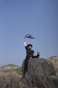 Woman standing on rock against blue sky