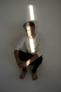 Portrait of young woman sitting against wall