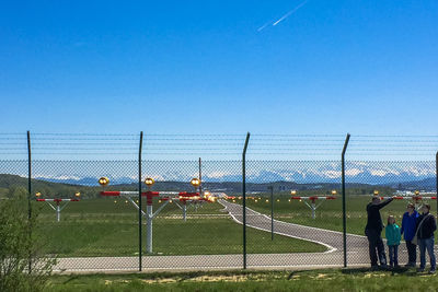 People on grassy field against clear blue sky