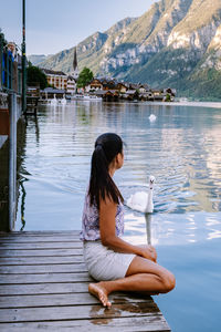 Side view of woman sitting on lake against mountain