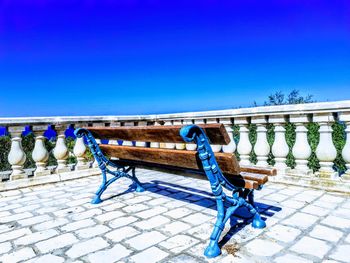 Bench in swimming pool against clear blue sky