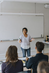 Teacher gesturing while teaching students sitting in classroom