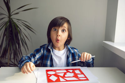 Boy child draws on paper with a ruler on a table sitting by the window