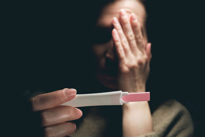 Cropped hand of woman holding cigarette against black background