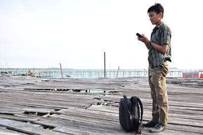 Young man using mobile phone in city against sky