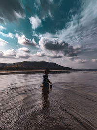 Rear view of boy in sea against sky