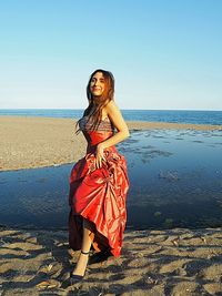 Portrait of young woman standing at beach against sky