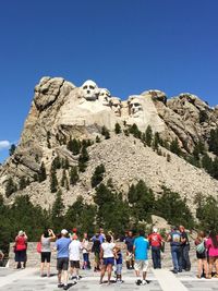 People on rock formation against clear blue sky
