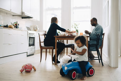 Father and mother having breakfast at dining table while daughter playing in dining room