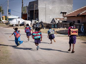 Rear view of schoolgirls running on street in town