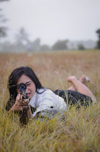 Young woman aiming gun while lying on grassy land