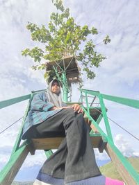 Low angle view of woman sitting against sky