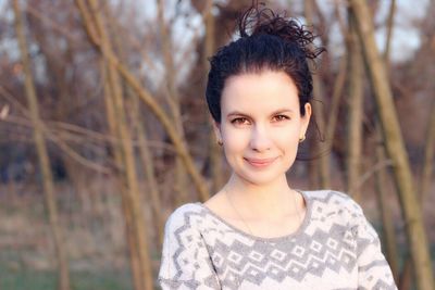 Portrait of confident young woman standing against bare trees