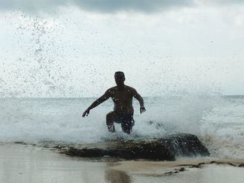 Silhouette man splashing water in sea against sky