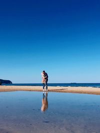 Man standing on beach against clear blue sky