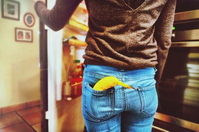 Rear view of woman with banana in pocket opening refrigerator door