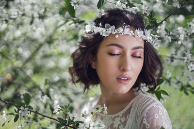 Portrait of a young beautiful woman in white clothes standing next to blooming cherry tree in spring