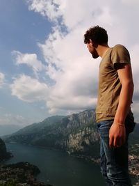 Side view of young man looking at mountain against sky