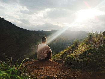 Rear view of man sitting on land against mountains and sky