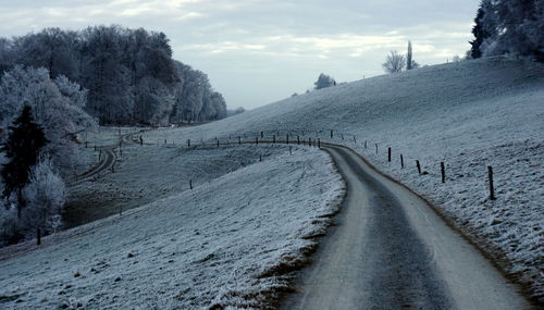 Snow covered road by mountains against sky