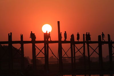 Silhouette people on u bein bridge over river during sunset