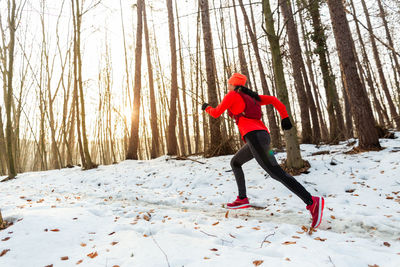 Female trail runner wearing hydration vest running uphill in forest on cold winter day.