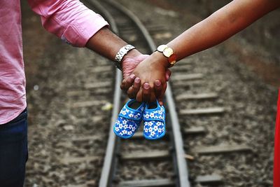 Cropped hand of couple holding baby booties over railroad track