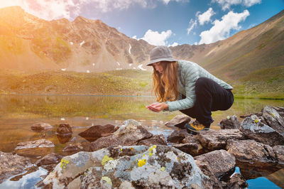 Young girl fills her hands with water from a stream of a cold mountain lake in order to drink and