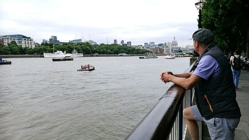 Man sailing on boat in river against sky in city