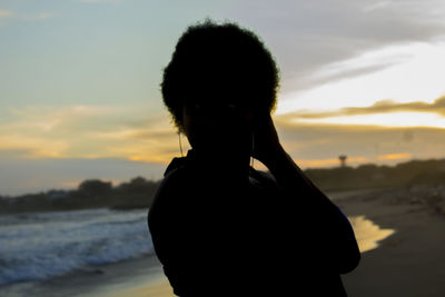 Silhouette woman standing at beach against sky during sunset