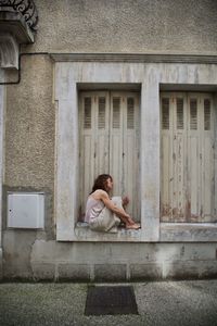 Side view of woman sitting against building