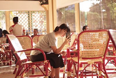 Woman photographing while sitting on chair at cafe