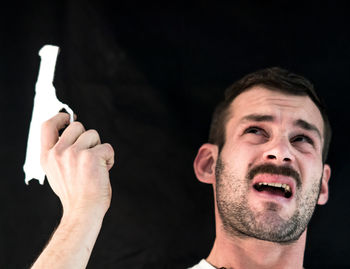 Shirtless man attempting suicide with gun against black background