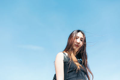 Low angle portrait of young woman standing against blue sky during sunny day