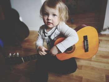 Portrait of cute girl playing guitar while sitting at home