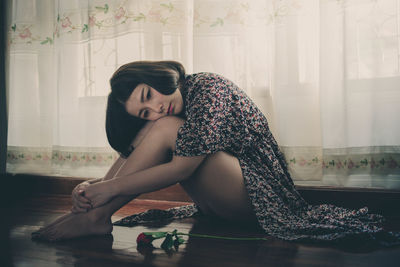 Sad woman sitting on floor by window at home