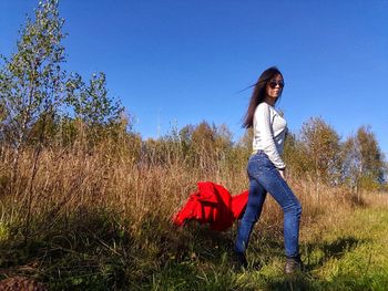 Full length of woman standing on field against clear blue sky