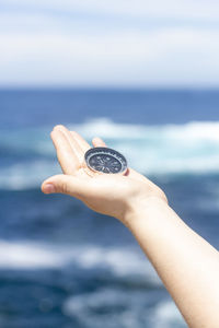 Cropped hand of woman holding navigational compass at beach