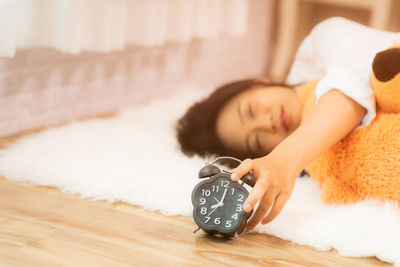 Woman holding alarm clock while lying on rug at home