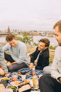 Happy male friends enjoying food during picnic against sky